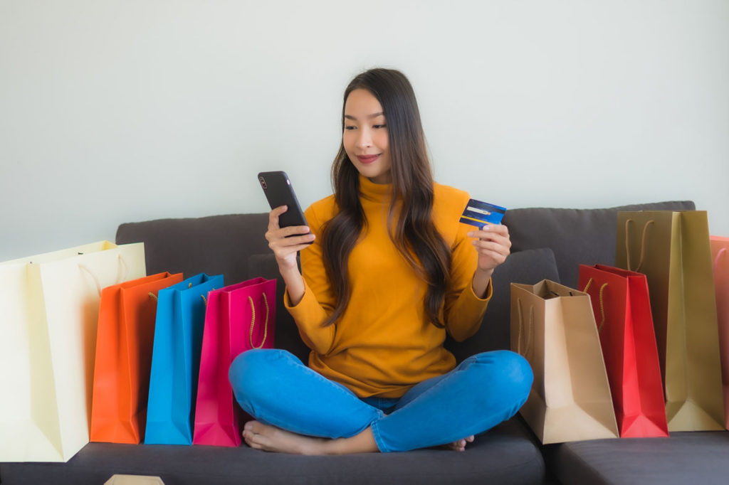 Retrato jovem mulher asiática usando computador portátil com telefone móvel esperto e cartão de crédito para compras on-line.