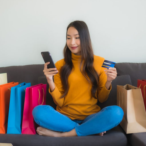 Retrato jovem mulher asiática usando computador portátil com telefone móvel esperto e cartão de crédito para compras on-line