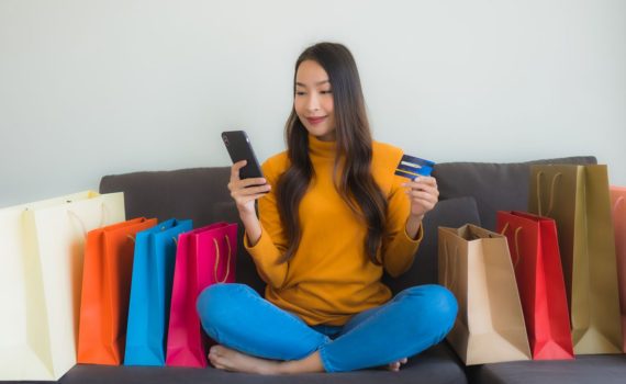 Retrato jovem mulher asiática usando computador portátil com telefone móvel esperto e cartão de crédito para compras on-line