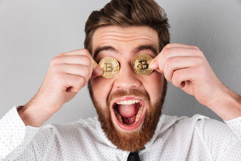 Jovem segura duas moedas douradas que representam a criptomoeda Bitcoin na altura dos olhos durante expressão de êxtase.