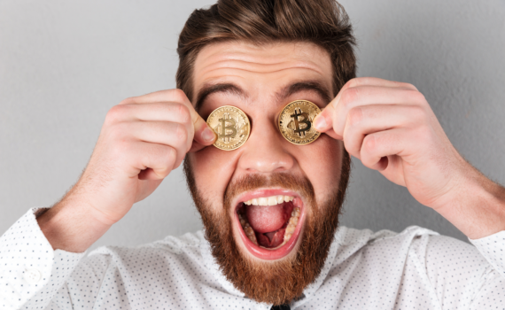 Jovem segura duas moedas de ouro que representam a criptomoeda Bitcoin na altura dos olhos enquanto mostra uma expressão de êxtase