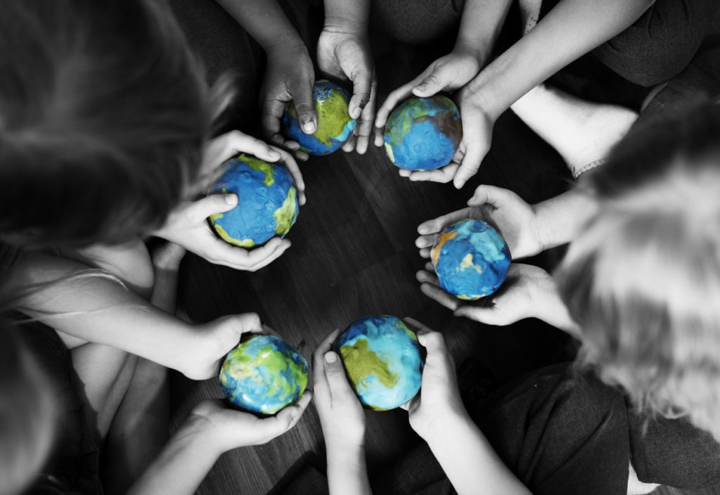 Roda de crianças em que cada uma segura nas mãos uma réplica do planeta Terra, simbolizando como o ser humano é sociável e possui uma bondade intrínseca.